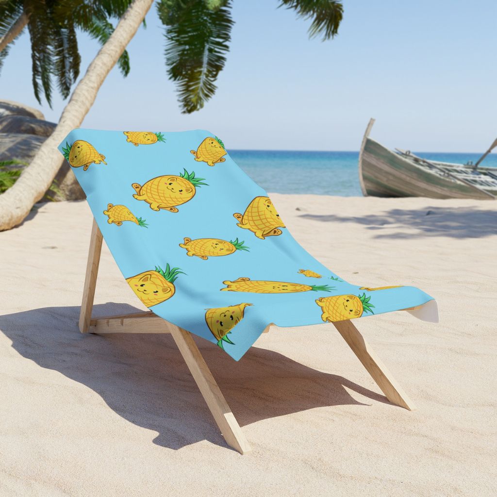 Light Blue Beach Towel with Pawnapple⢠print on a sunchair on sandy beach. Pawnapple⢠is a pineapple drawn as a cute cat.