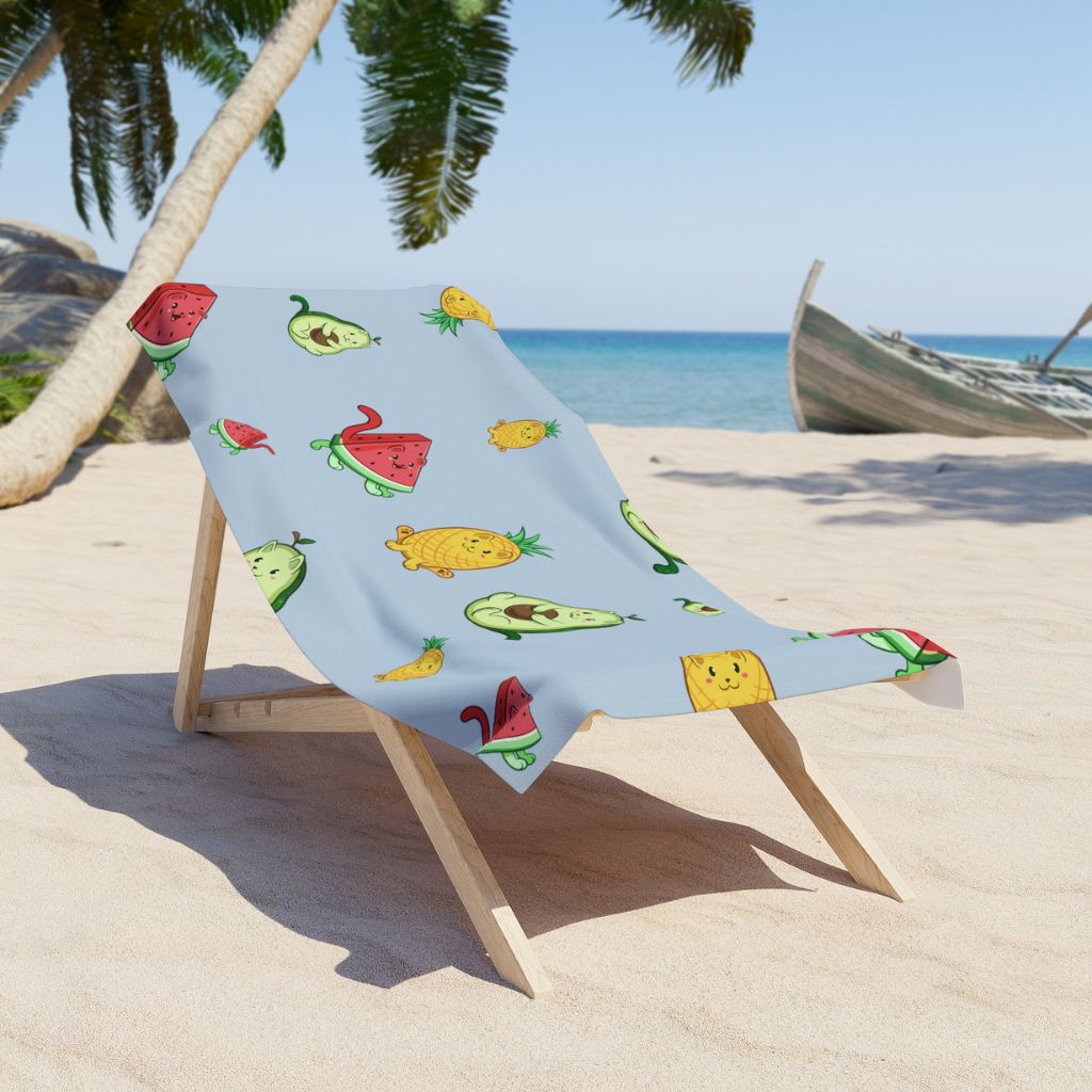 Light Blue Beach Towel with Fruitkittens⢠logo on a sunchair on sandy beach. Fruitkittens⢠are fruits drawn as cute cats. The logo features Pawocadoâ˘, Pawnapple⢠and Watermewlonâ˘