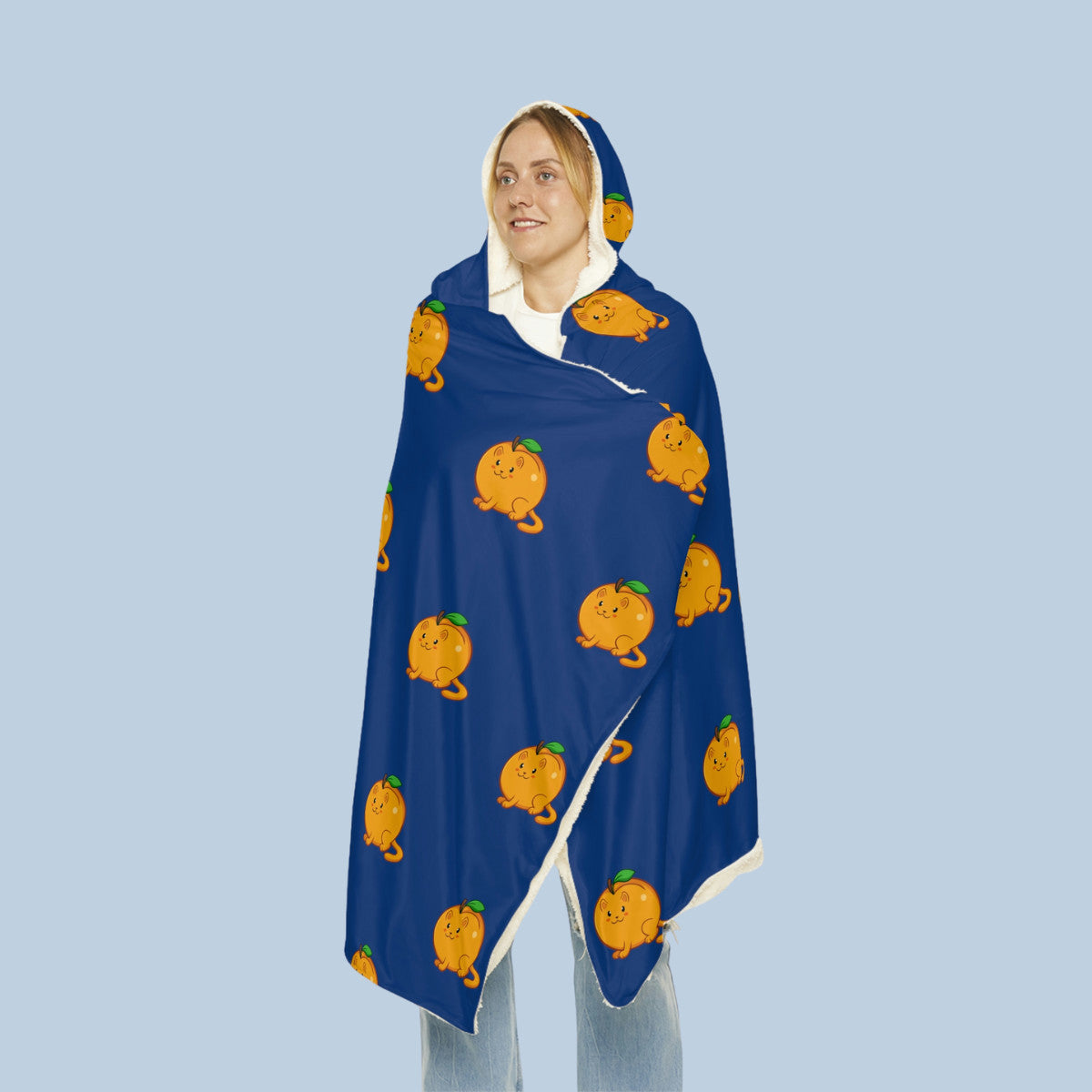 Happy woman wearing the dark blue Apricat⢠hooded microfiber fleece blanket seen from front. Apricat⢠is an apricot drawn as a cute cat.