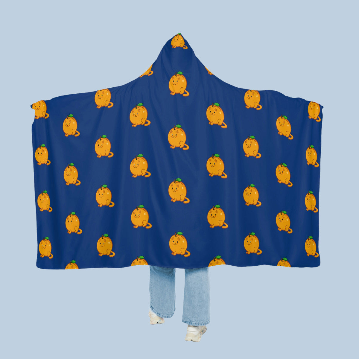 Happy woman wearing the dark blue Apricat⢠hooded microfiber fleece blanket like a cape with arms stretched out seen from behind so that the full pattern is visible. Apricat⢠is an apricot drawn as a cute cat.
