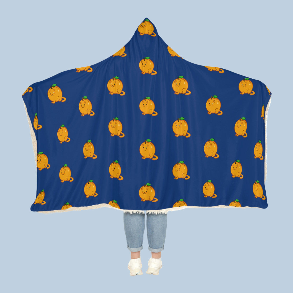 Happy woman wearing the dark blue Apricat⢠hooded sherpa blanket like a cape with arms stretched out seen from behind so that the full pattern is visible. Apricat⢠is an apricot drawn as a cute cat.