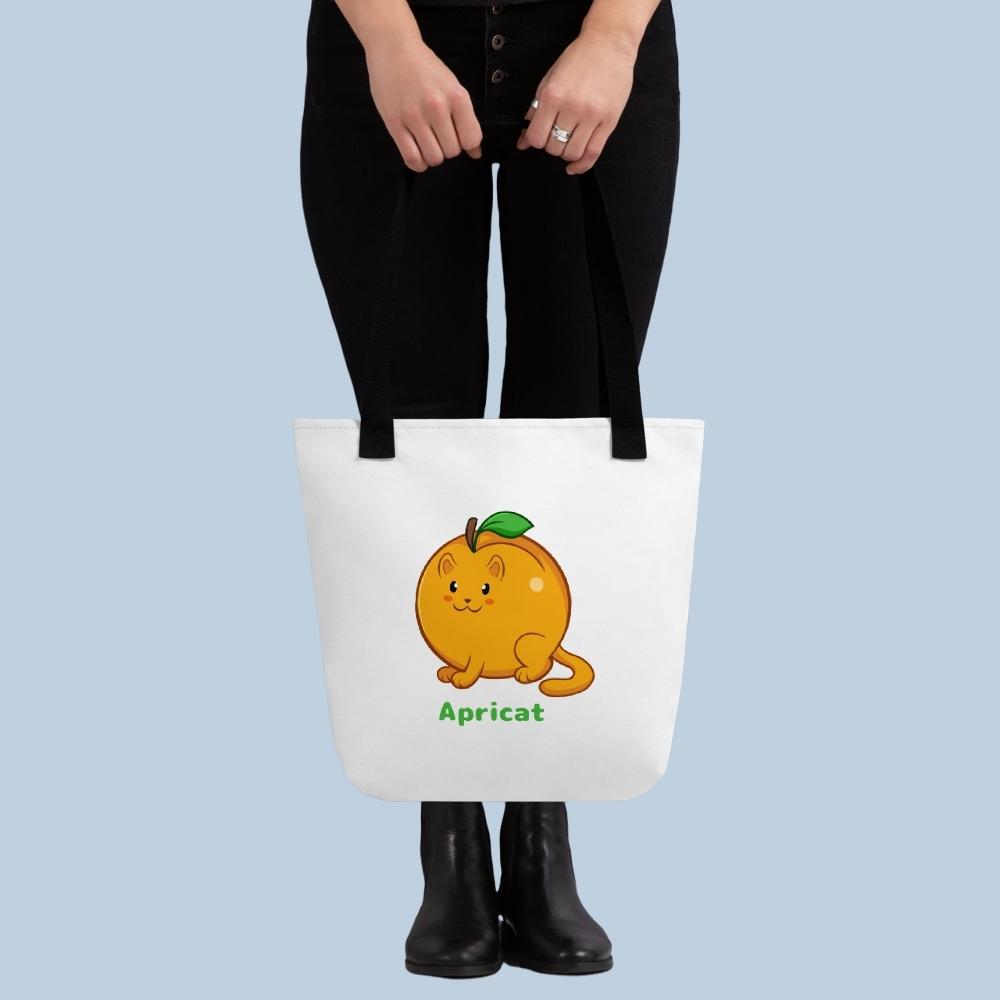 Person holding a white Tote Bag with Apricat⢠print. Apricat⢠is an apricot drawn as a cute cat.