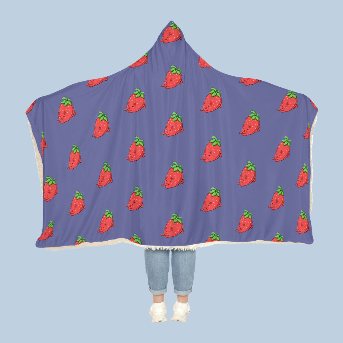 Happy woman wearing the purple Clawberry⢠hooded sherpa blanket like a cape with arms stretched out seen from behind so that the full pattern is visible. Clawberry⢠is a strawberry drawn as a cute cat.
