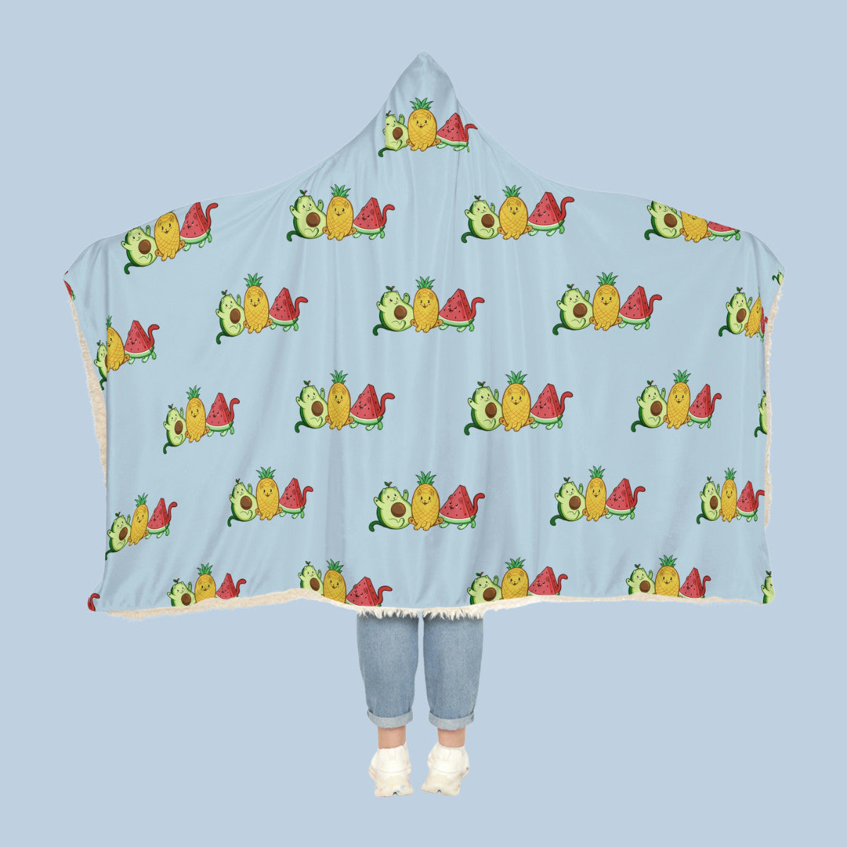 Happy woman wearing the light blue Fruitkittens⢠logo hooded sherpa blanket like a cape with arms stretched out seen from behind so that the full pattern is visible. Fruitkittens⢠are fruits drawn as cute cats. The logo features Pawocadoâ˘, Pawnapple⢠and Watermewlonâ˘