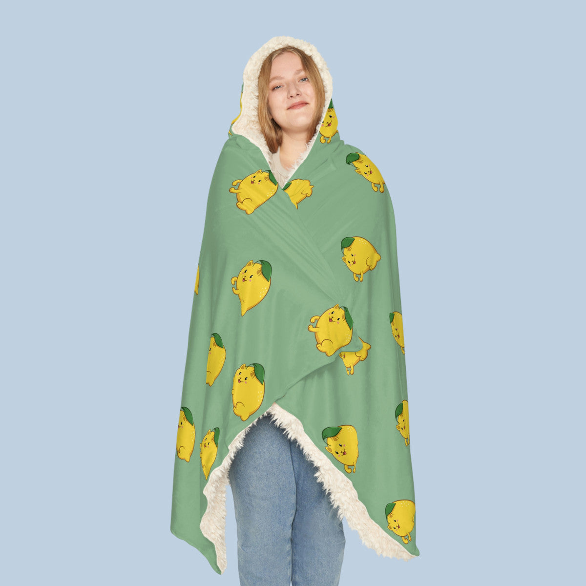 Happy woman wearing the light green Lemeow⢠hooded sherpa blanket seen from front. Lemeow⢠is a lemon drawn as a cute cat.