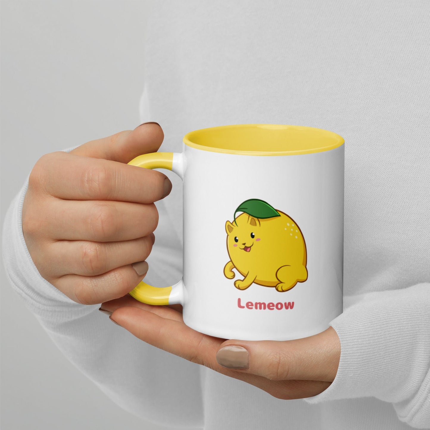 Hands holding a white and yellow Coffee Mug with Lemeow⢠print. Lemeow⢠is a lemon drawn as a cute cat.