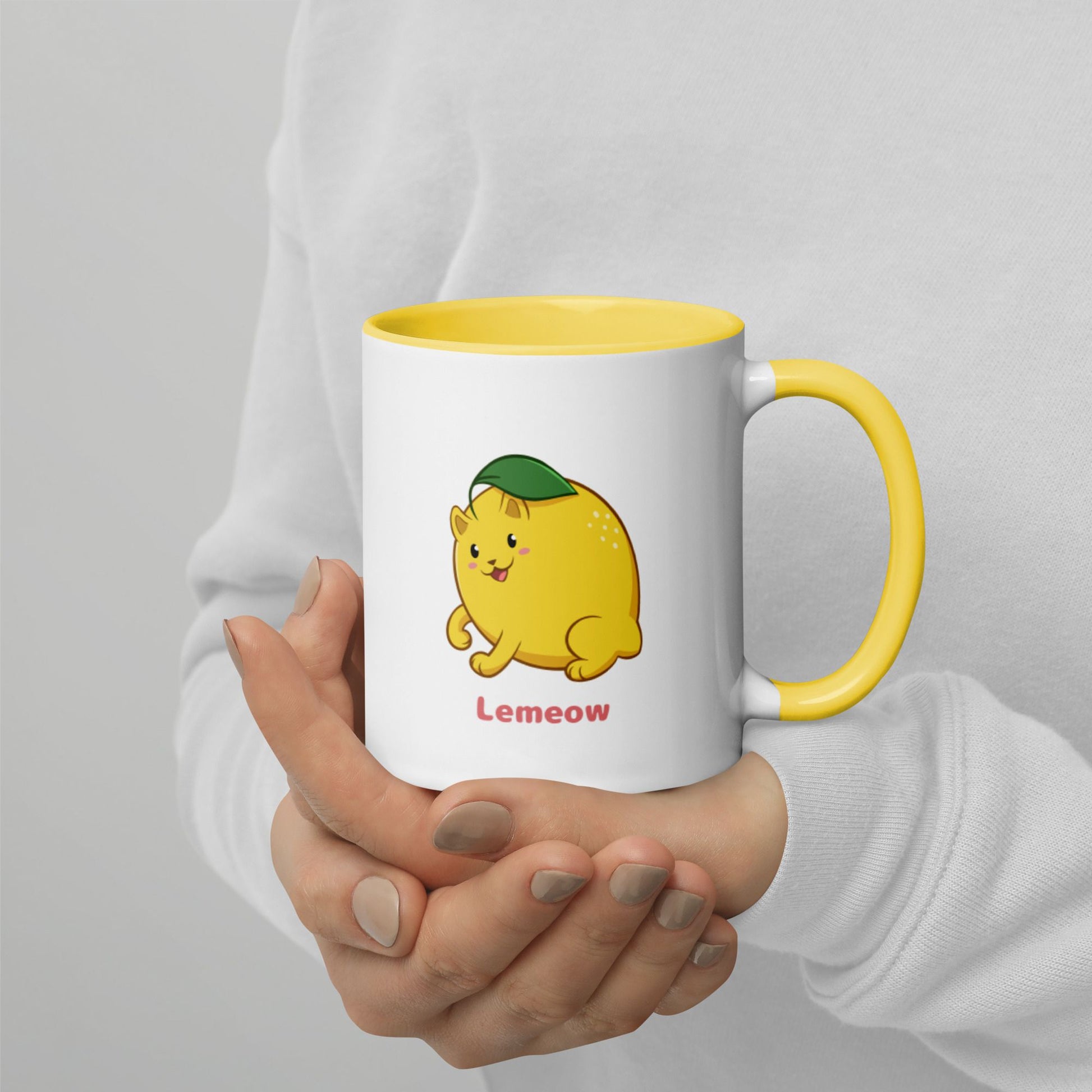 Hands holding a white and yellow Coffee Mug with Lemeow⢠print. Lemeow⢠is a lemon drawn as a cute cat.