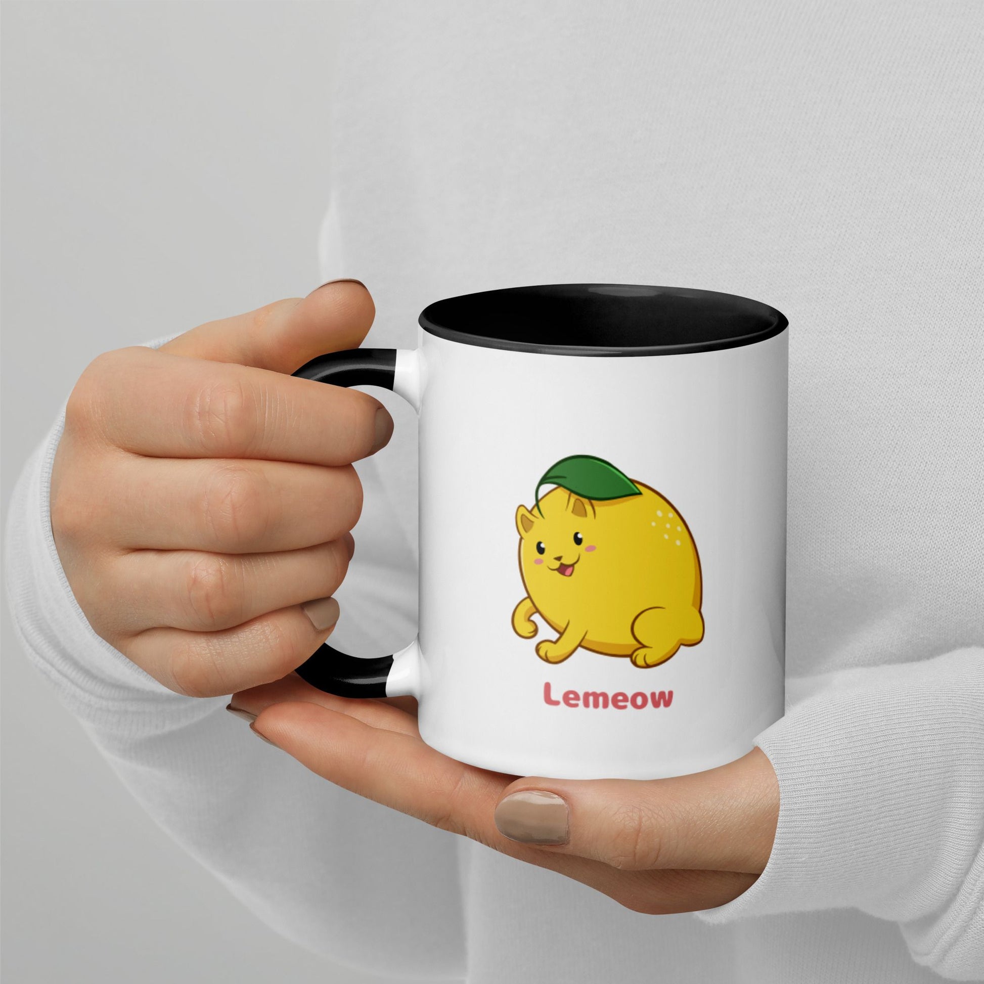 Hands holding a white and black Coffee Mug with Lemeow⢠print. Lemeow⢠is a lemon drawn as a cute cat.