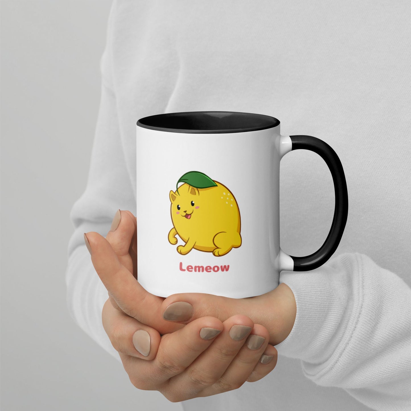 Hands holding a white and black Coffee Mug with Lemeow⢠print. Lemeow⢠is a lemon drawn as a cute cat.