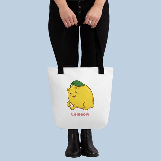 Person holding a white Tote Bag with Lemeow⢠print. Lemeow⢠is a lemon drawn as a cute cat.