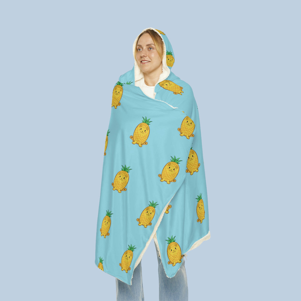 Happy woman wearing the light blue Pawnapple⢠hooded microfiber fleece blanket seen from front. Pawnapple⢠is a pineapple drawn as a cute cat.