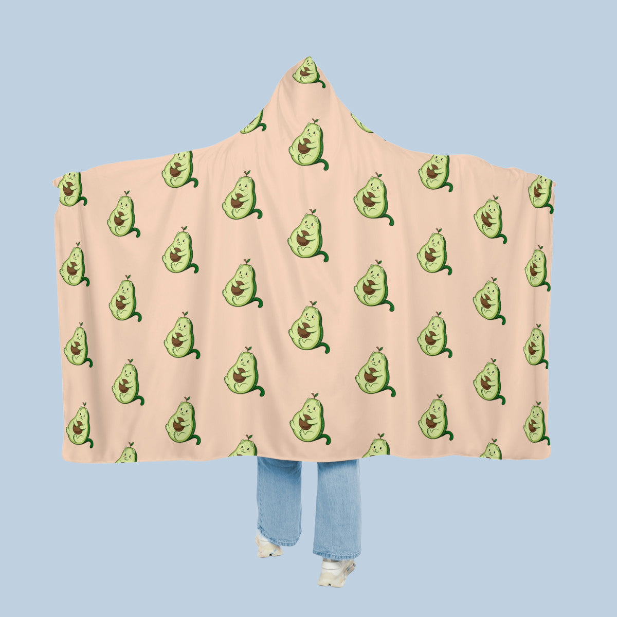Happy woman wearing the beige Pawocado⢠hooded microfiber fleece blanket like a cape with arms stretched out seen from behind so that the full pattern is visible. Pawocado⢠is an avocado drawn as a cute cat.