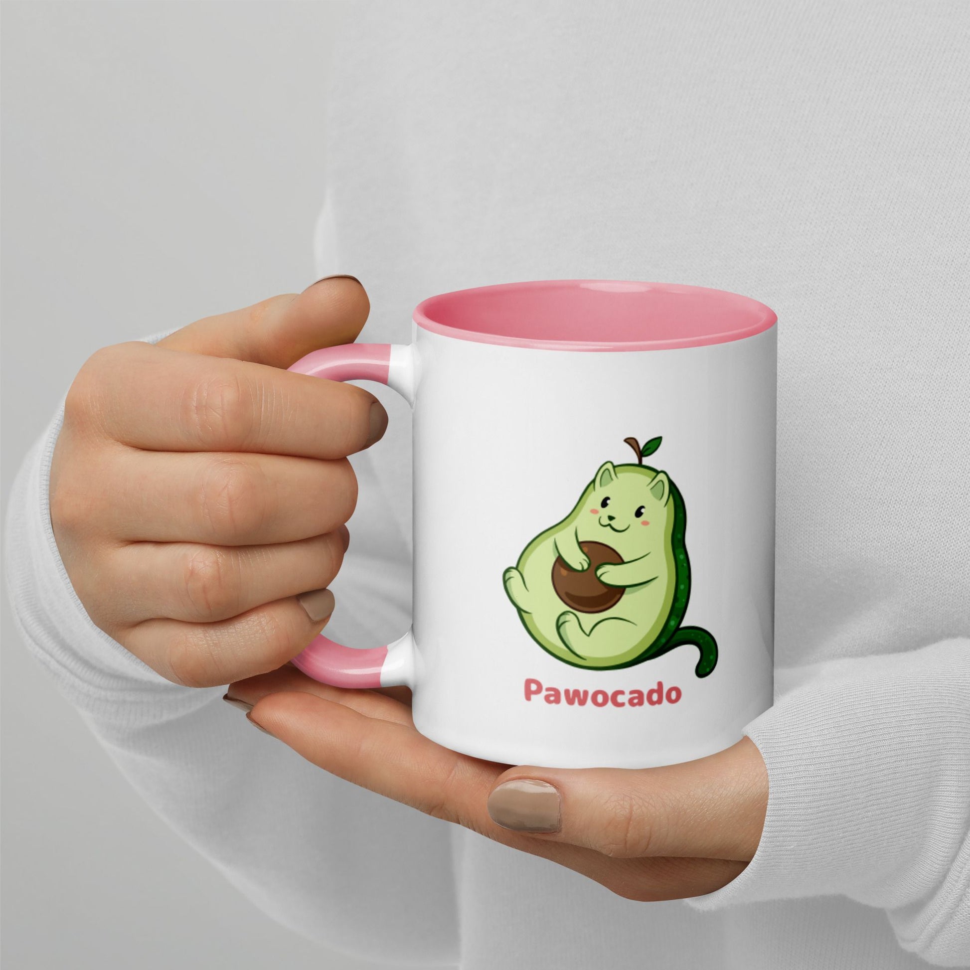 Hands holding a white and pink Coffee Mug with Pawocado⢠print. Pawocado⢠is an avocado drawn as a cute cat.