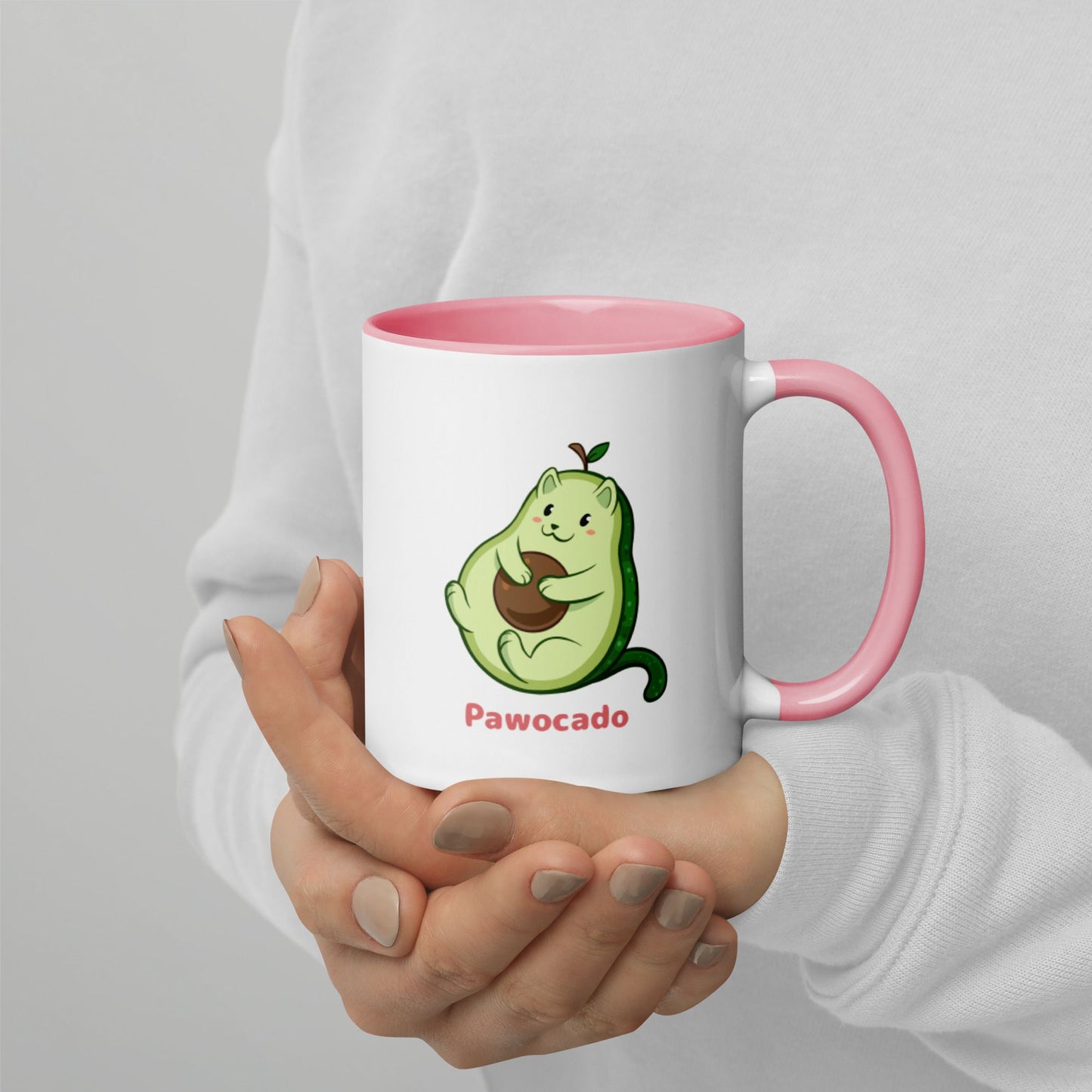 Hands holding a white and pink Coffee Mug with Pawocado⢠print. Pawocado⢠is an avocado drawn as a cute cat.