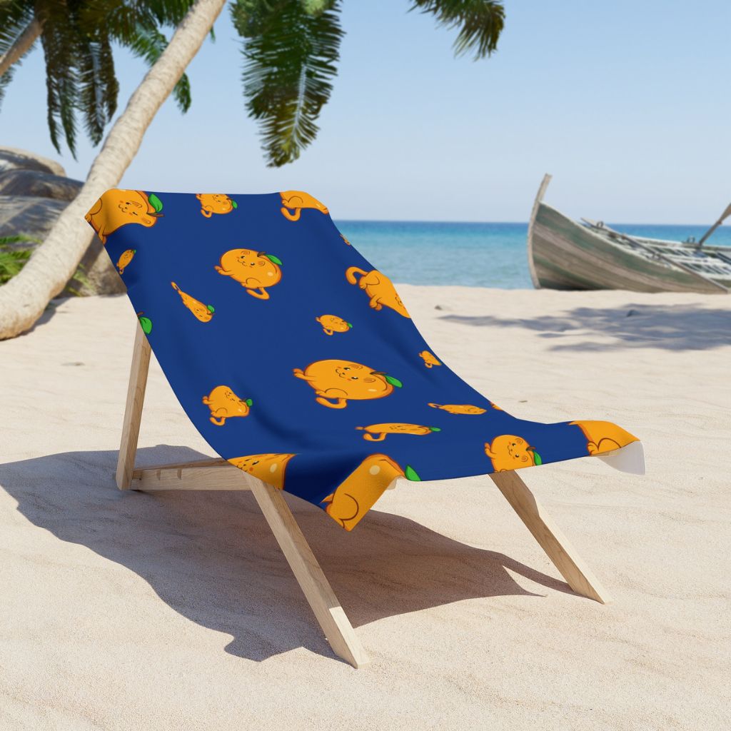 Dark Blue Beach Towel with Apricat™ print on a sunchair on sandy beach. Apricat™ is an apricot drawn as a cute cat.