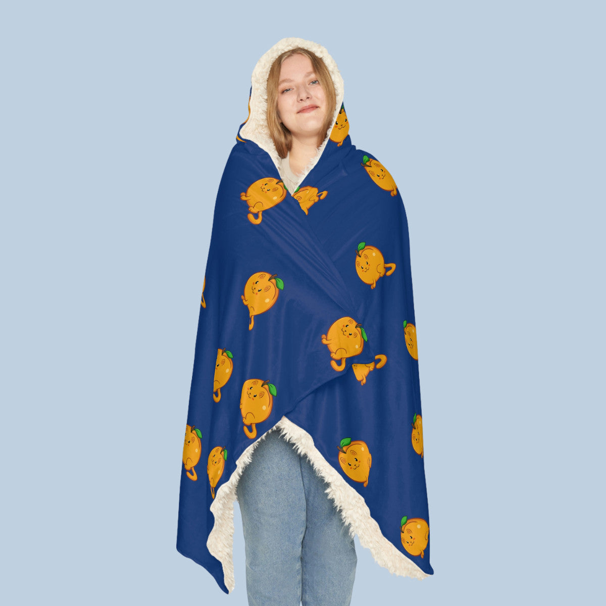 Happy woman wearing the dark blue Apricat™ hooded sherpa blanket seen from front. Apricat™ is an apricot drawn as a cute cat.