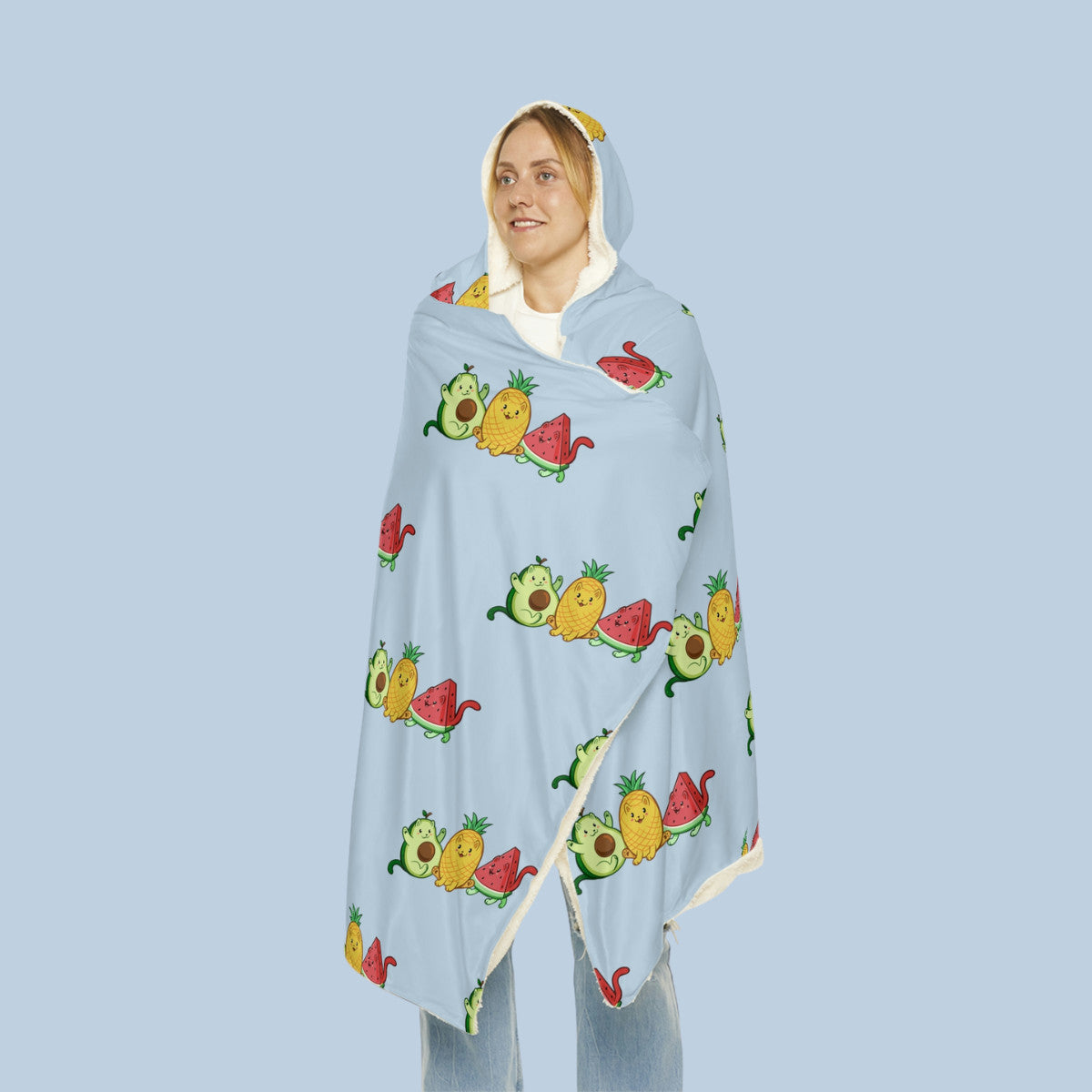 Happy woman wearing the light blue Fruitkittens™ logo hooded microfiber fleece blanket seen from front. Fruitkittens™ are fruits drawn as cute cats. The logo features Pawocado™, Pawnapple™ and Watermewlon™