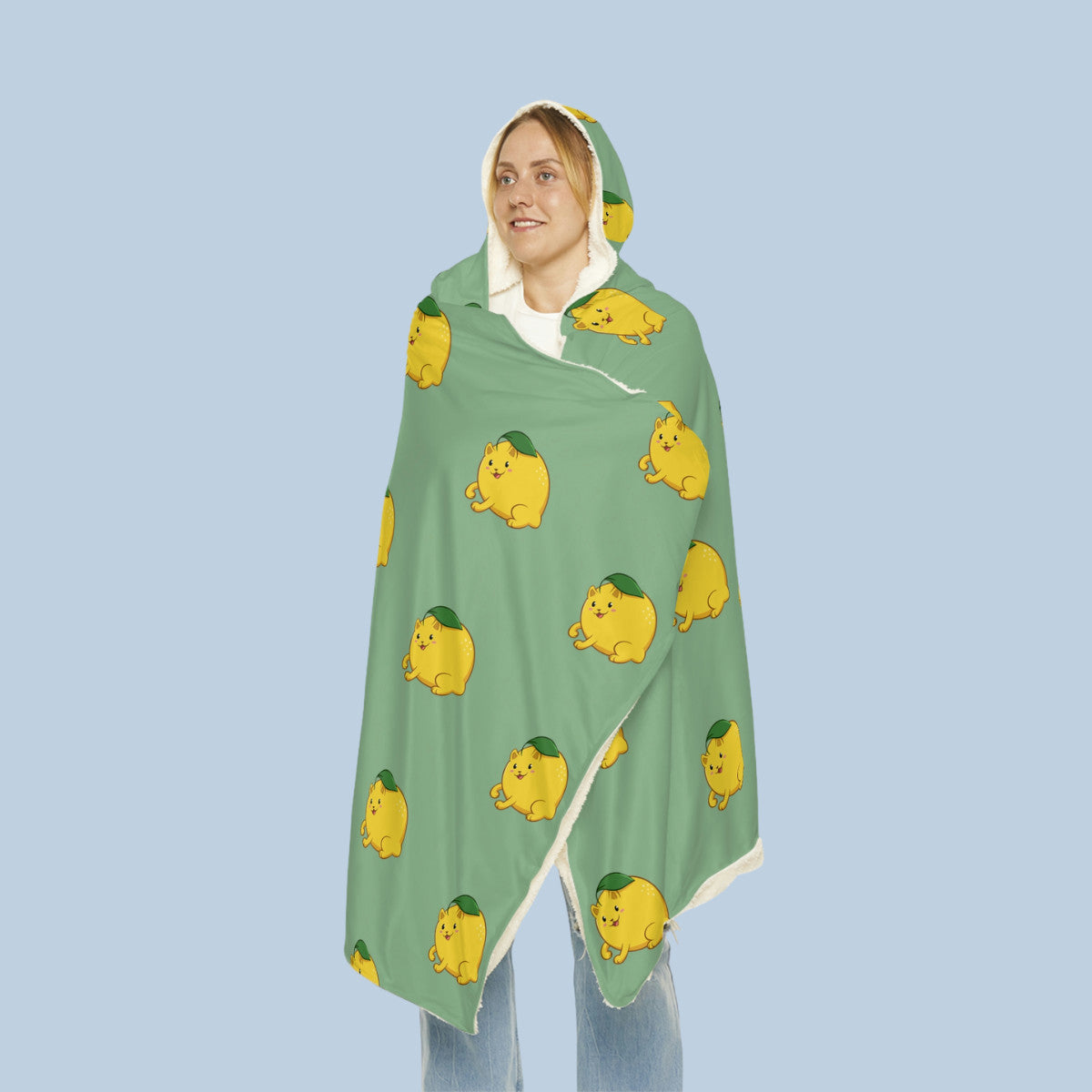 Happy woman wearing the light green Lemeow™ hooded microfiber fleece blanket seen from front. Lemeow™ is a lemon drawn as a cute cat.