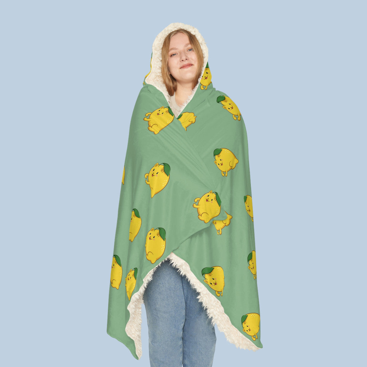 Happy woman wearing the light green Lemeow™ hooded sherpa blanket seen from front. Lemeow™ is a lemon drawn as a cute cat.