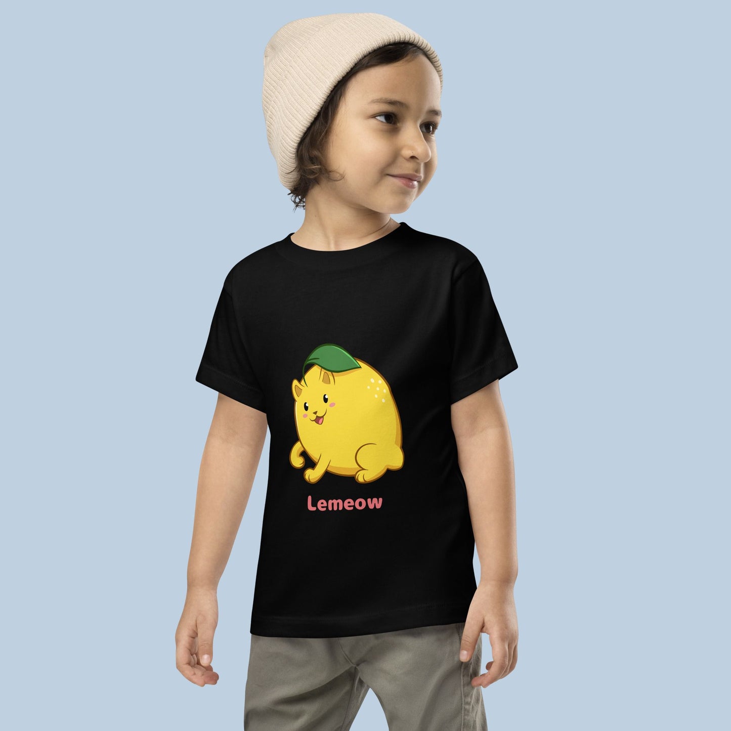 Toddler wearing a black Toddler T-Shirt with Lemeow™ print. Lemeow™ is a lemon drawn as a cute cat.