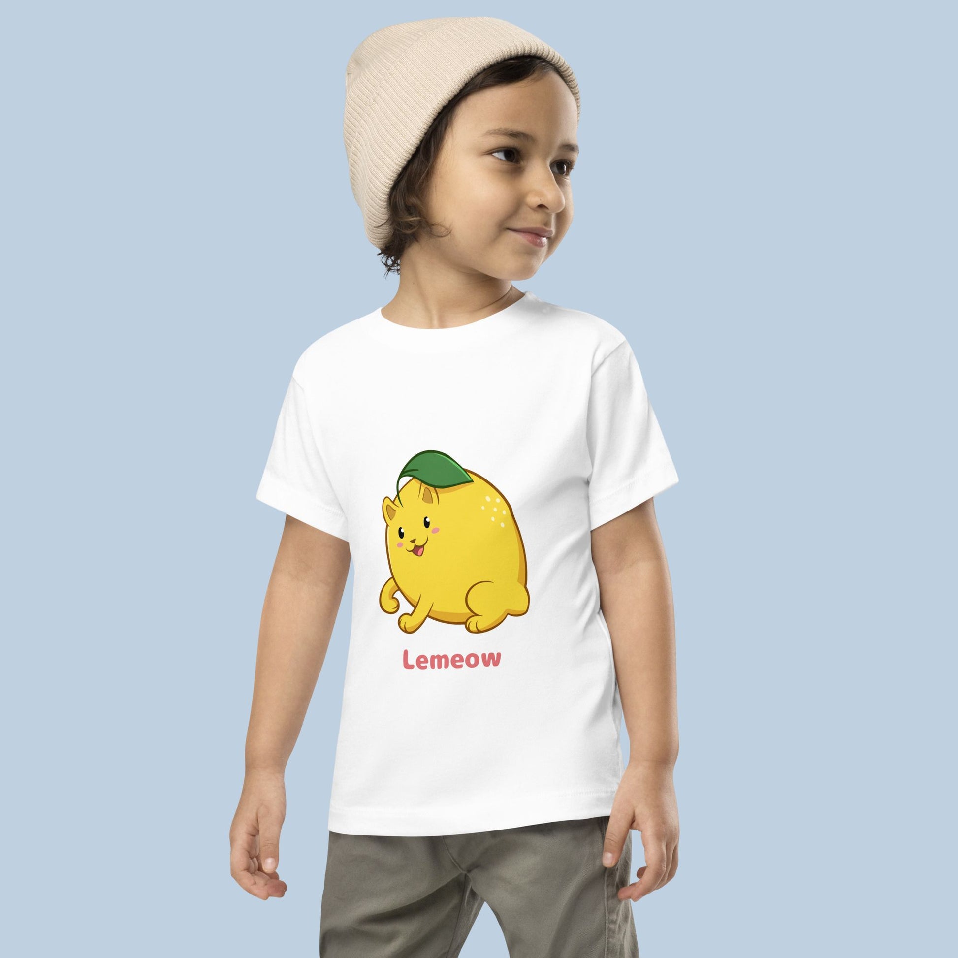 Toddler wearing a white Toddler T-Shirt with Lemeow™ print. Lemeow™ is a lemon drawn as a cute cat.