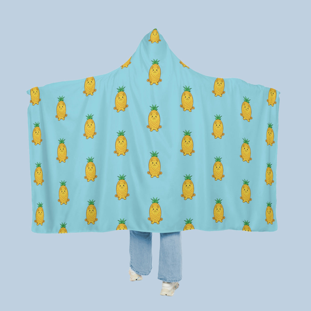 Happy woman wearing the light blue Pawnapple™ hooded microfiber fleece blanket like a cape with arms stretched out seen from behind so that the full pattern is visible. Pawnapple™ is a pineapple drawn as a cute cat.