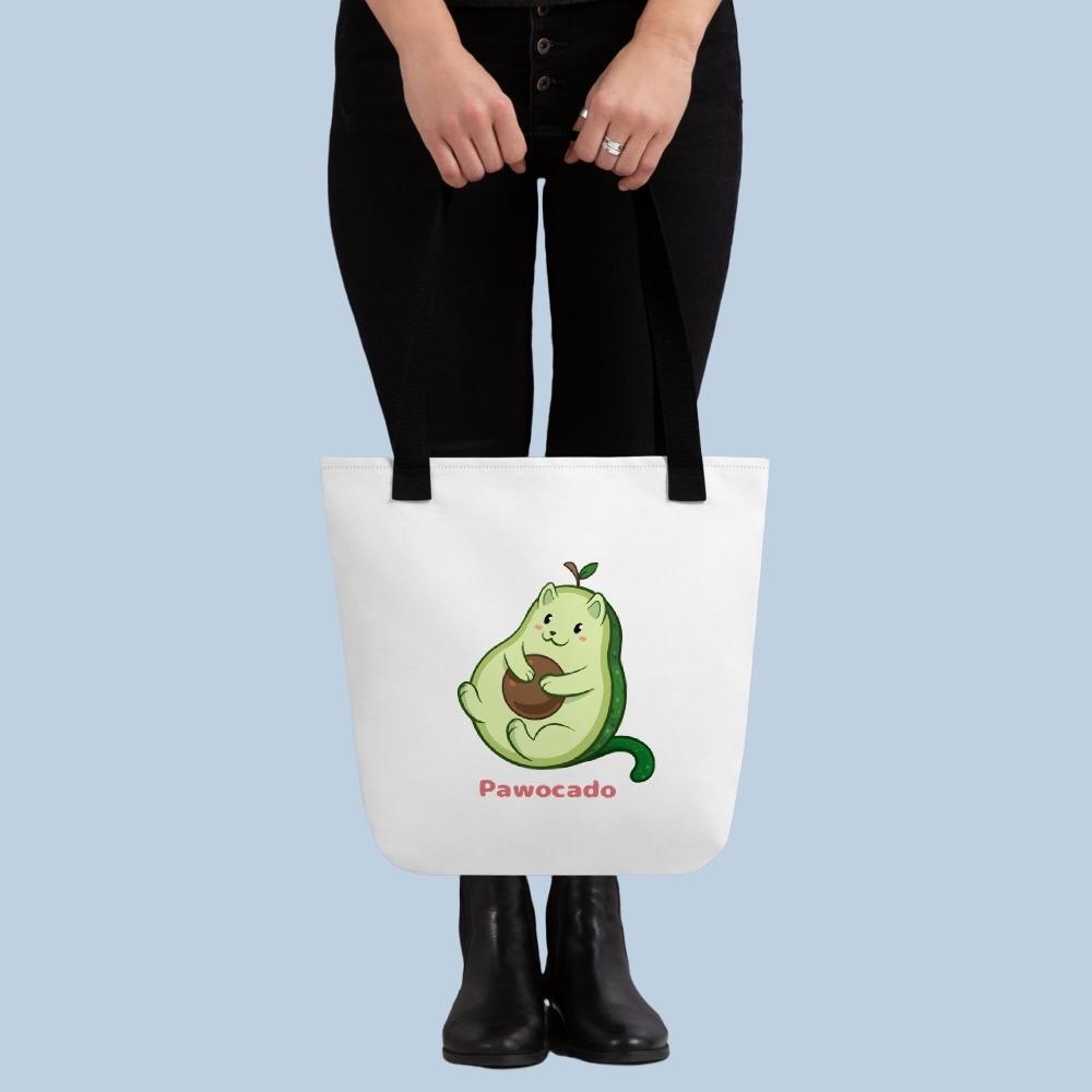 Person holding a white Tote Bag with Pawocado™ print. Pawocado™ is an avocado drawn as a cute cat.